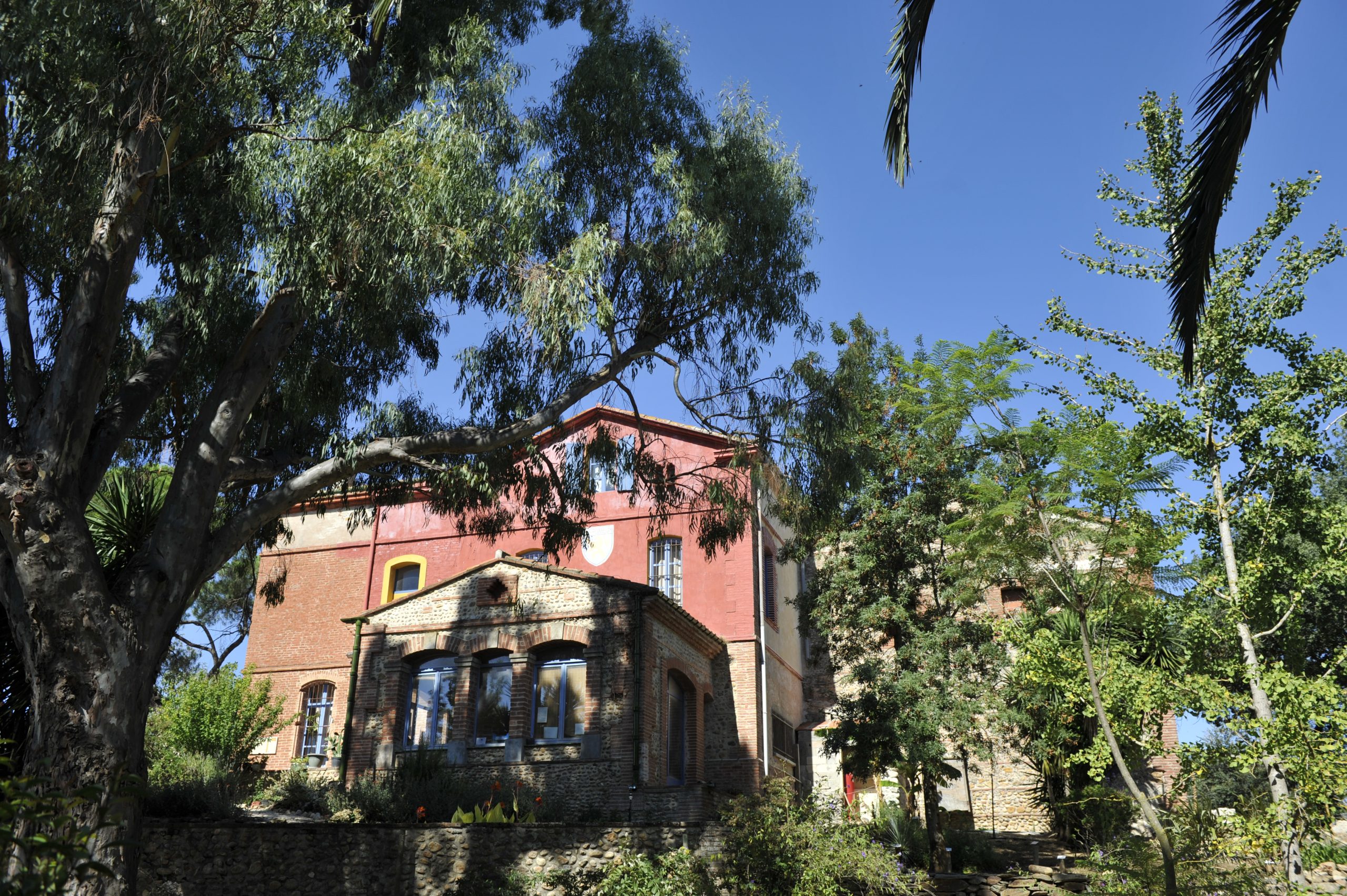View of the Arboretum Mas Roussillon in Canet-en-Roussillon, part of the AIS network, with the historic building surrounded by Mediterranean vegetation.